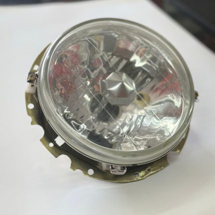 It features a clear lens with a multi-surface reflector design. The assembly includes a metal mounting or adjustment bracket. The headlight is compatible with a halogen H4 bulb type. It is often used as an aftermarket upgrade for older vehicles.