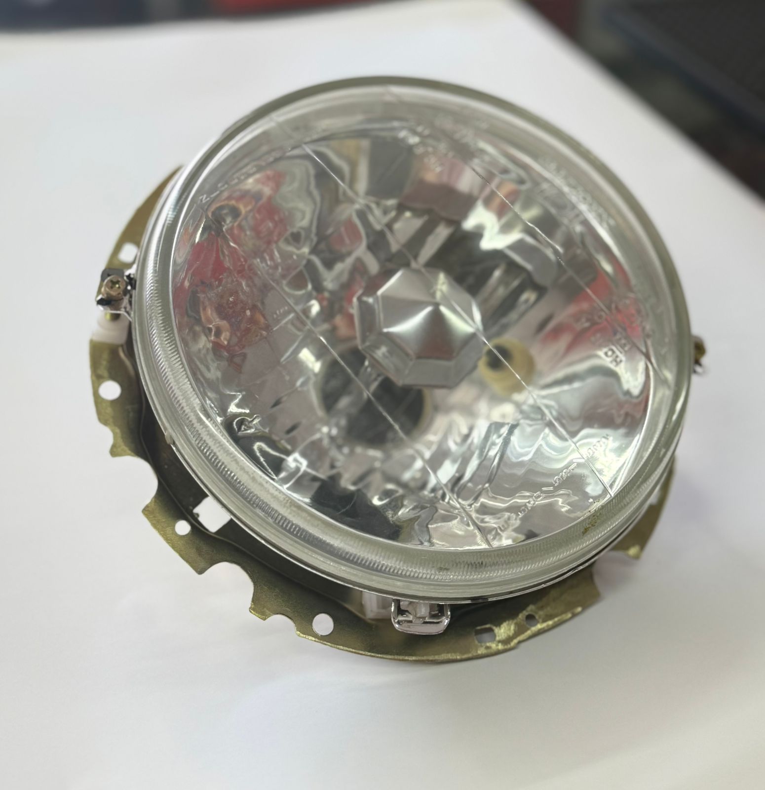 VW GOLF 1 CRYSTAL CROSS OUTER HEAD LIGHT It features a clear lens with a multi-surface reflector design. The assembly includes a metal mounting or adjustment bracket. The headlight is compatible with a halogen H4 bulb type. It is often used as an aftermarket upgrade for older vehicles.